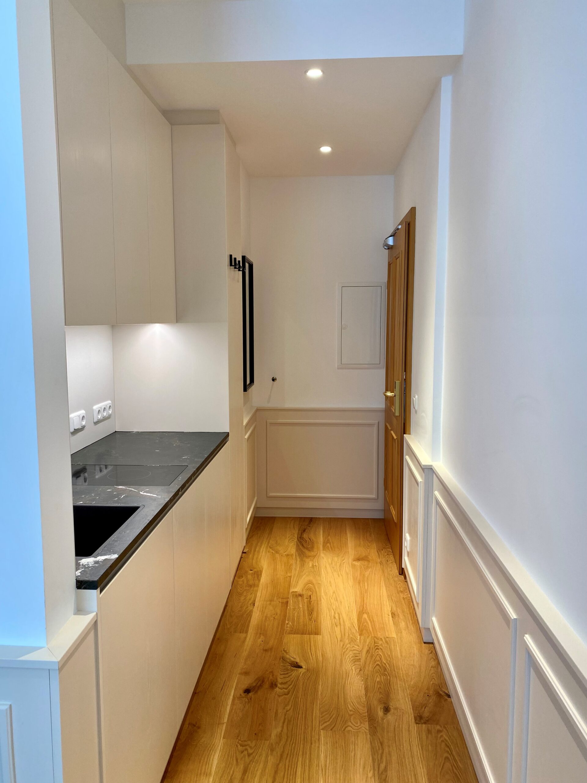 Hotel room hallway with kitchenette and wooden flooring
