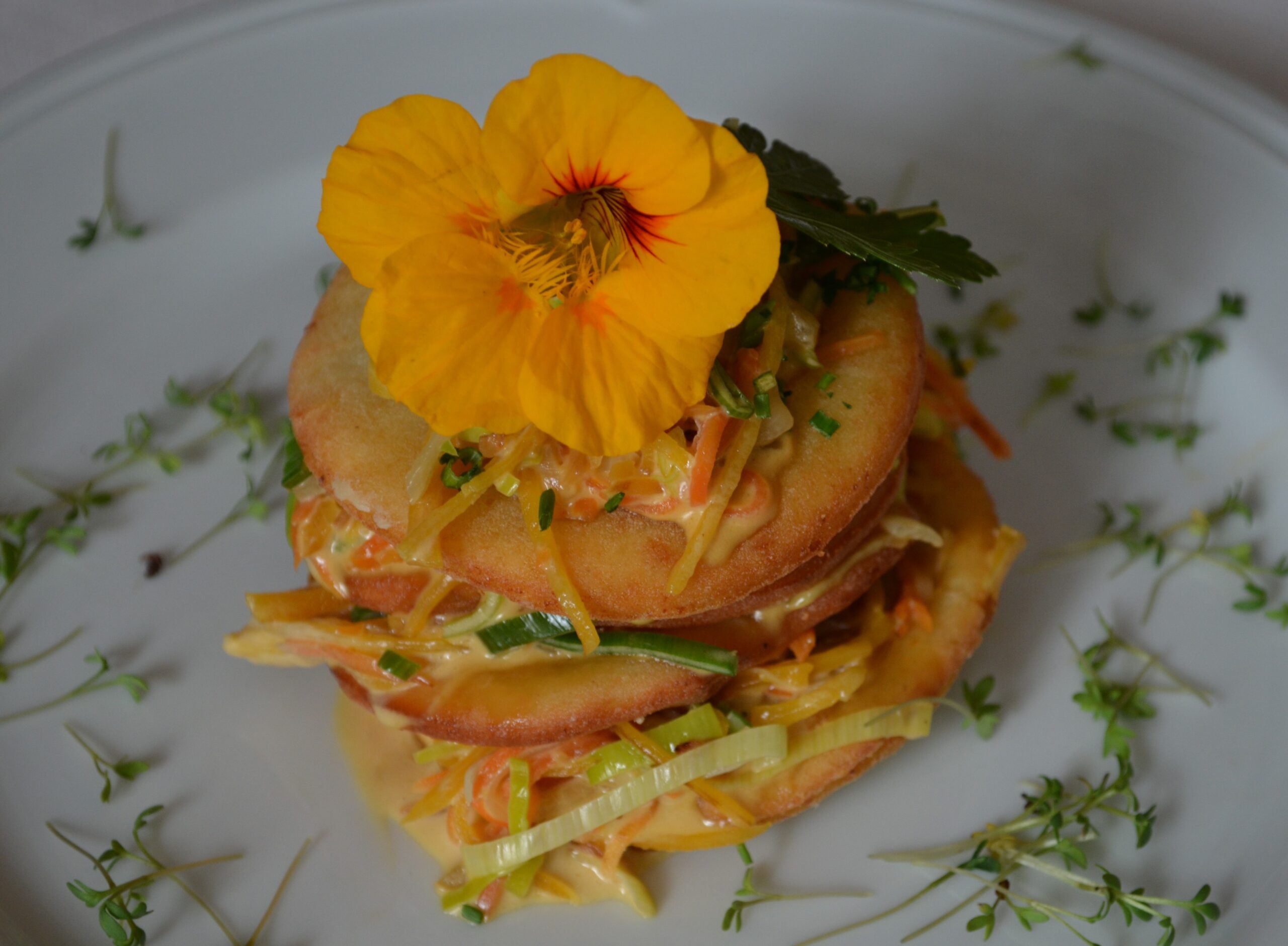 Layered vegetable and potato dish garnished with edible flowers
