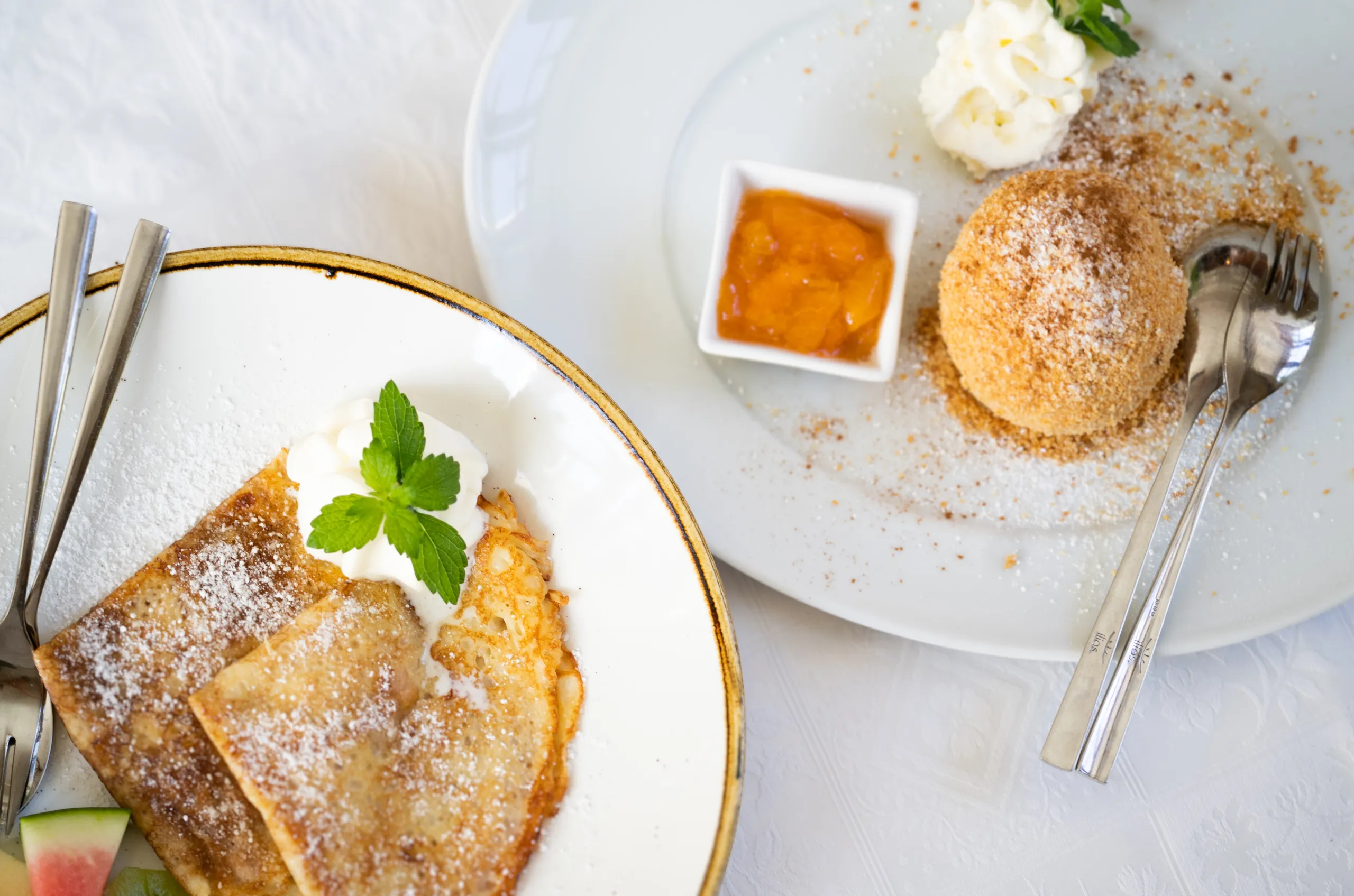 Nahaufnahme von Palatschinken mit Staubzucker und einer Marillenknödel mit Kompott.