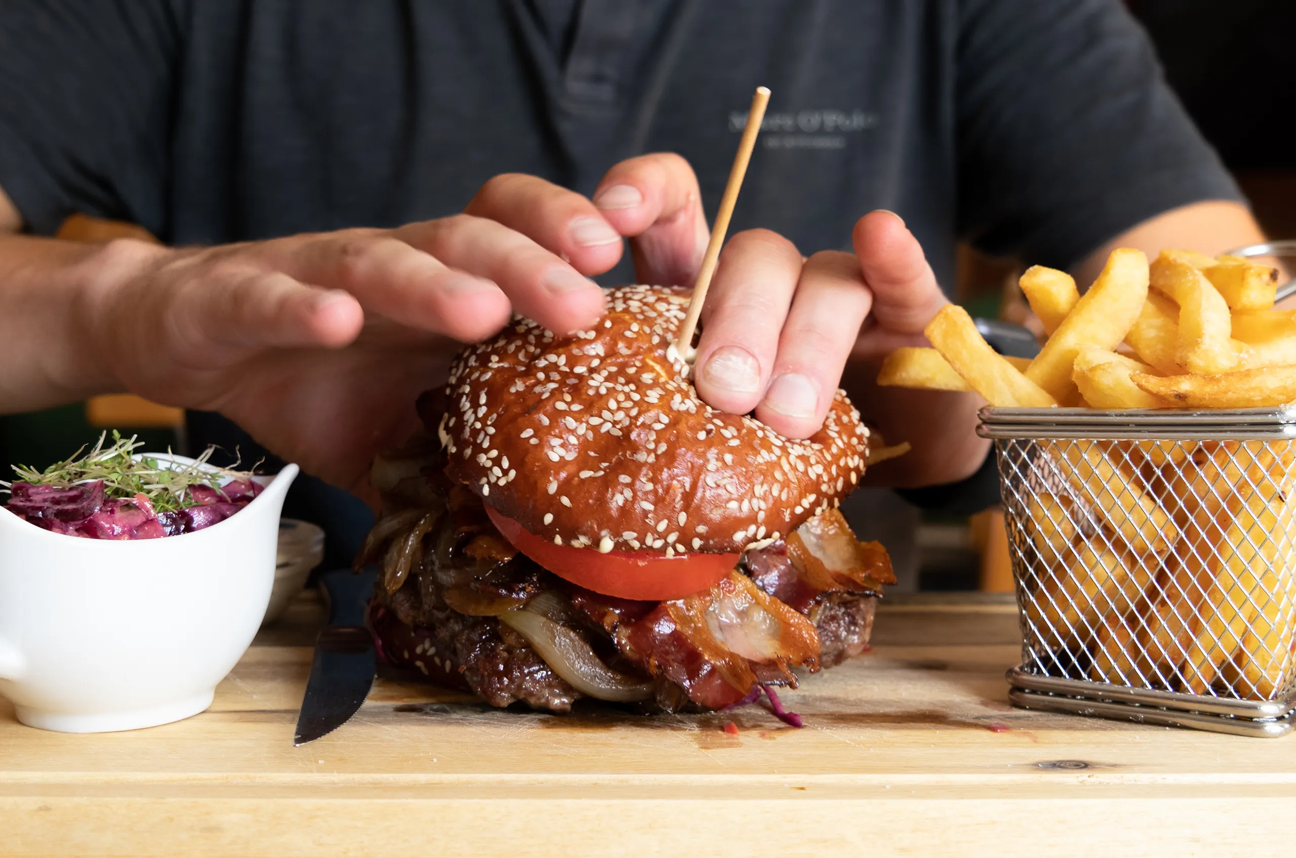 Saftiger Burger mit Sesam-Brioche, Speck, Zwiebeln und Pommes frites.