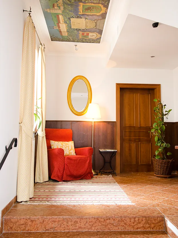 Gemütlicher Eingangsbereich mit rotem Sessel, Stehlampe, Spiegel und dekorierter Decke.
