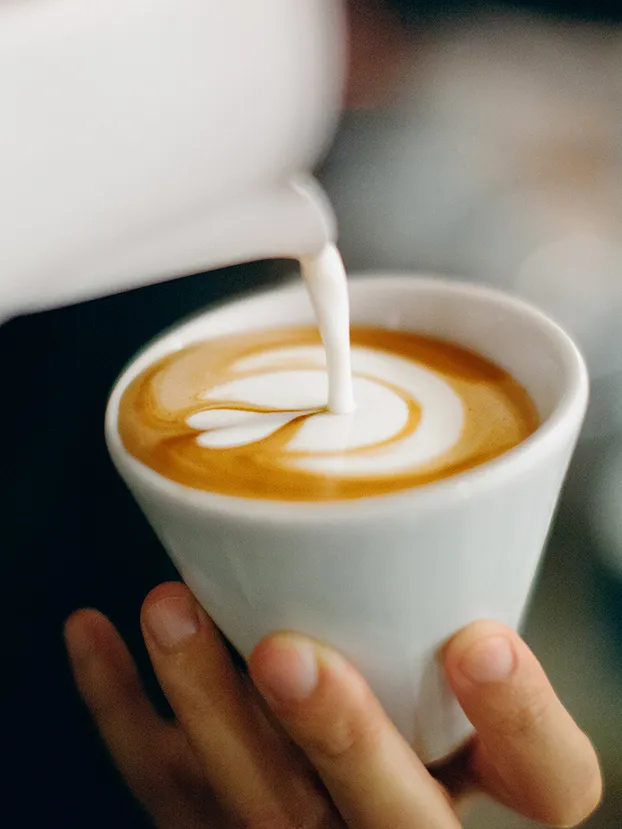Nahaufnahme eines Cappuccinos, in den Milch für Latte Art eingegossen wird.
