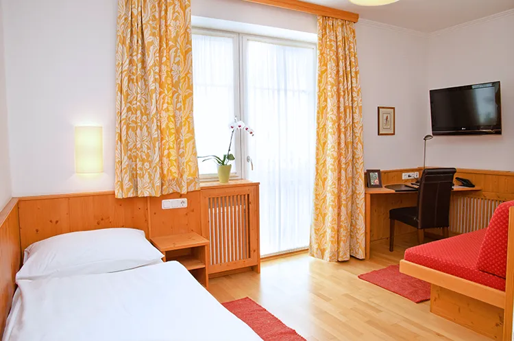 Helles Hotelzimmer mit gelben Vorhängen, Holzwänden und Schreibtischbereich.