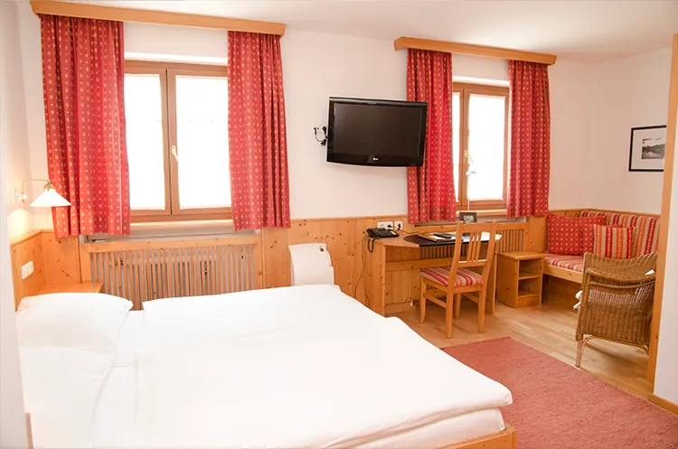 Helles Hotelzimmer mit roten Vorhängen, Doppelbett, Schreibtisch und Sitzbereich.