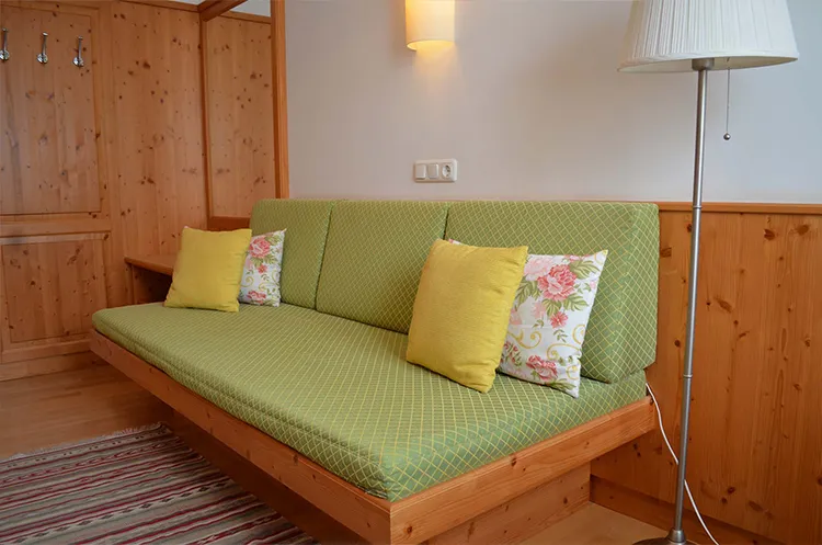 Grüne Couch mit Deko-Kissen in einem gemütlichen Hotelzimmer mit Holzelementen.