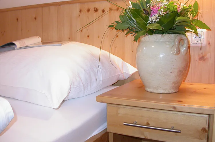 Nahaufnahme eines Hotelbetts mit weißen Kissen und einer Blumenvase am Nachttisch.