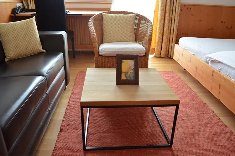 Sitzbereich mit Sofa, Korbstuhl und modernem Couchtisch auf rotem Teppich.