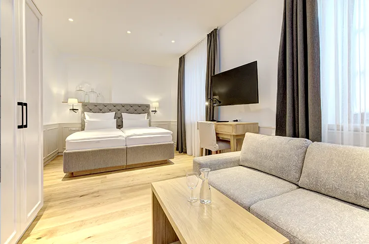 Großzügiges Hotelzimmer mit Doppelbett, Sofa und hellem Holzinterieur.