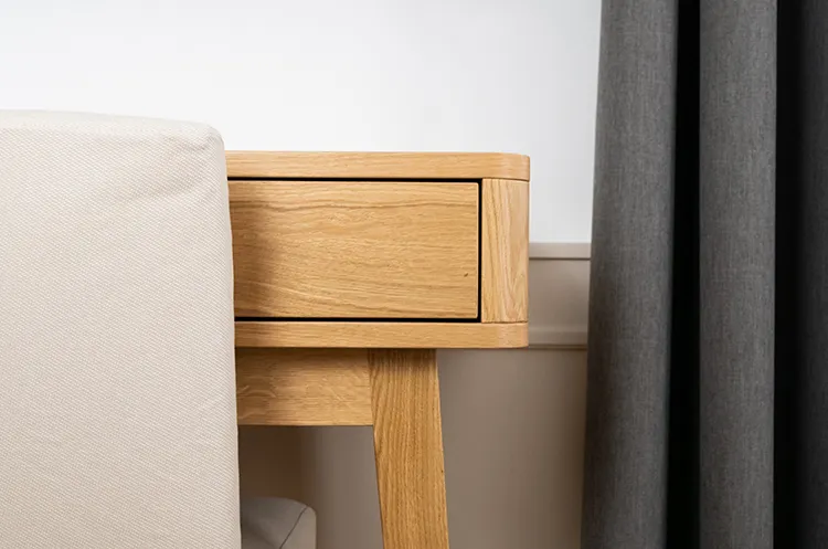 Nahaufnahme eines hellen Holzschreibtisches neben einem Stuhl und grauen Vorhängen.