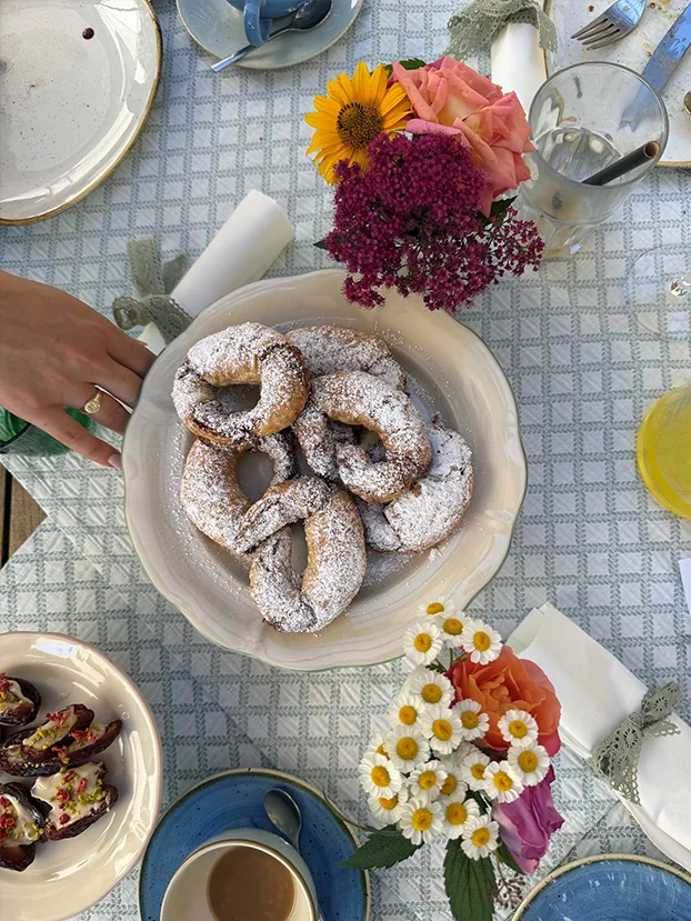 Hausgemachte Kipferl mit Staubzucker auf einem gedeckten Frühstückstisch mit Blumen.